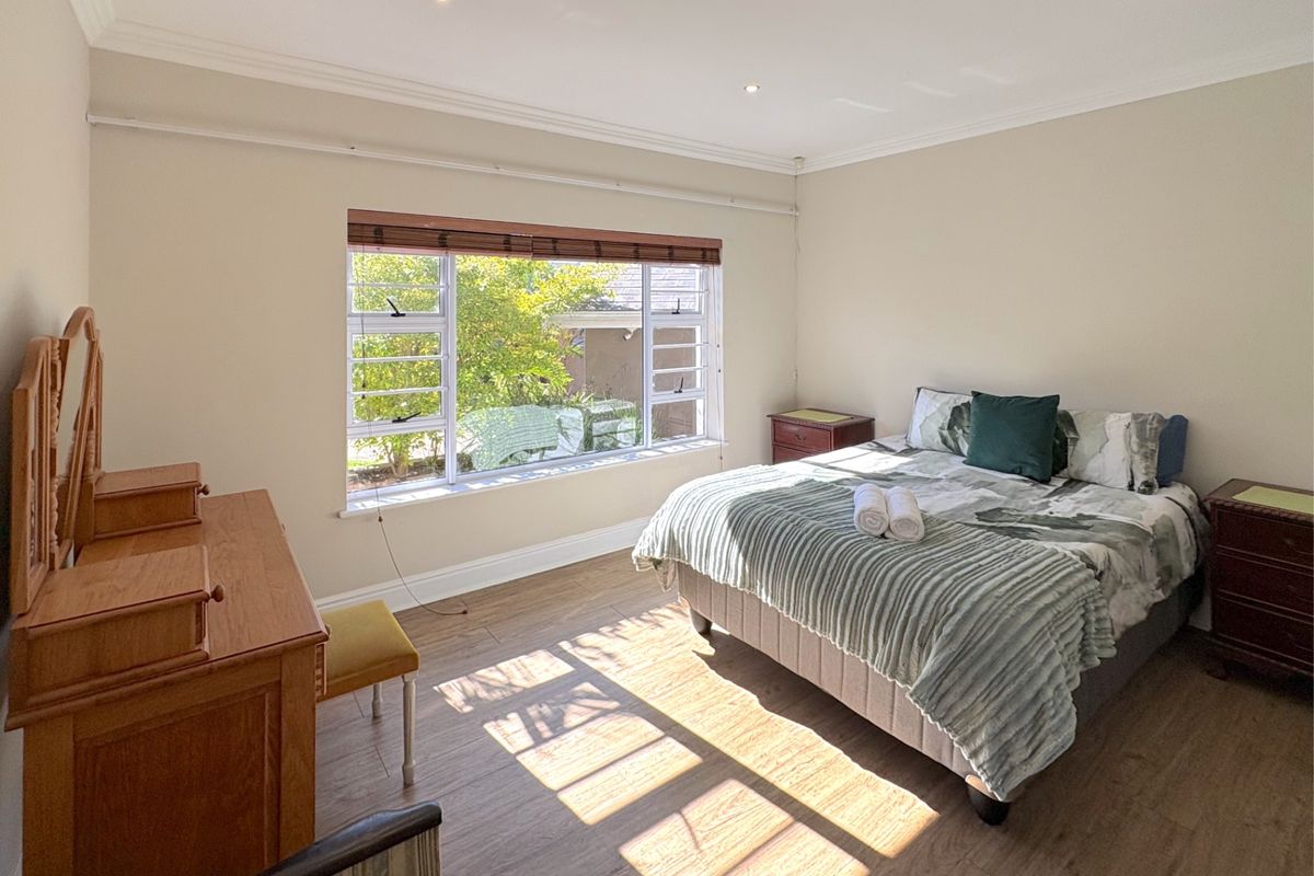 A well-lit bedroom featuring laminate flooring, recessed downlights, and large windows with timber frames, offering a bright and comfortable living space.