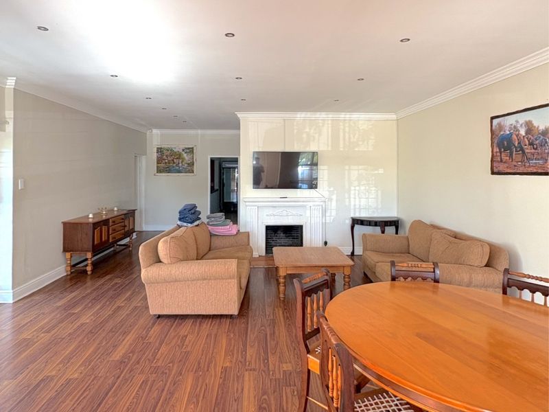 Spacious open-plan living and dining area featuring laminate flooring, recessed lighting, crown molding, and a central fireplace.