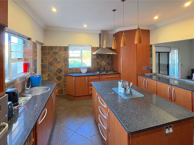 Spacious kitchen featuring wooden cabinetry, granite countertops, a central island, and a built-in gas hob with stainless steel extractor fan.