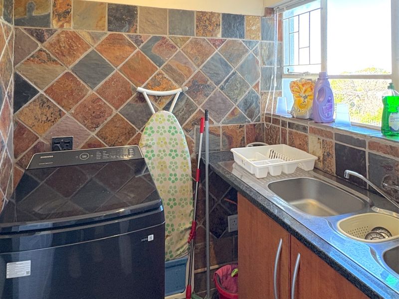 Functional laundry area featuring a stainless steel double sink, granite countertops, and distinctive slate tile splashback with ample storage cabinetry.