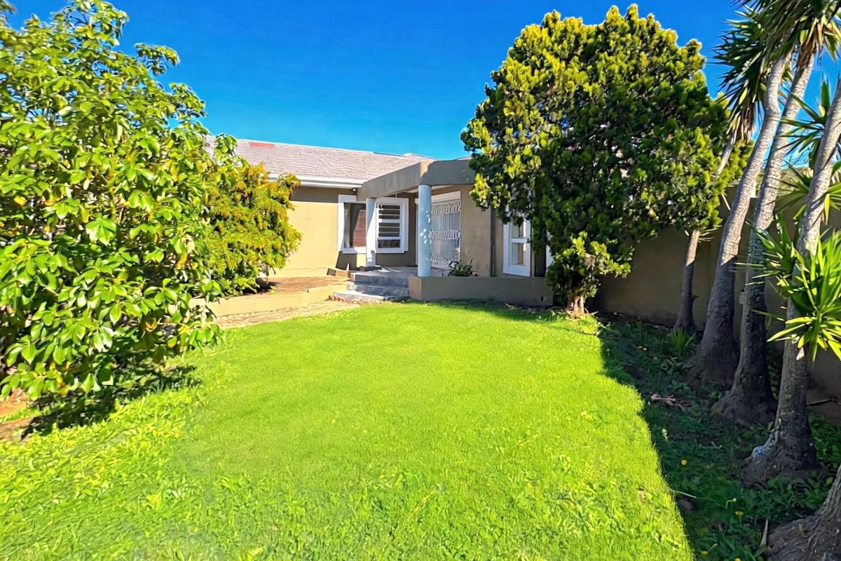 A rear view of the house featuring a small covered patio area, established garden, and secure boundary walls.