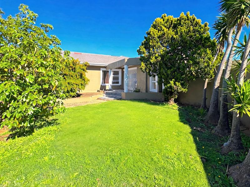 A rear view of the house featuring a small covered patio area, established garden, and secure boundary walls.
