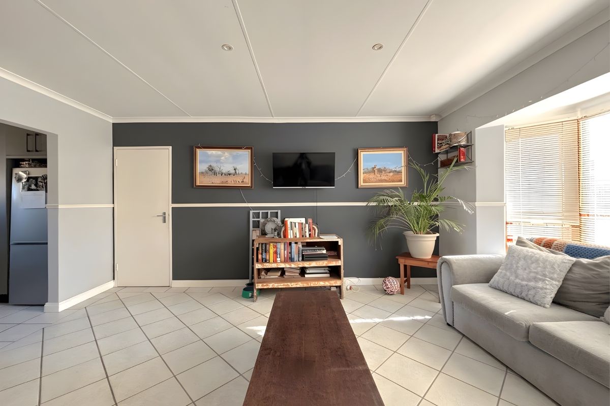 A spacious living room featuring tiled flooring, a dark accent wall, and a large bay window allowing for natural light.