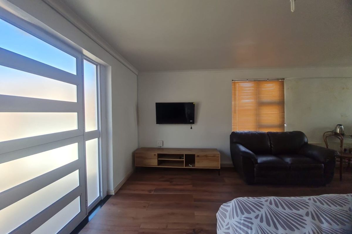 A living room featuring wood-look flooring, a large glass panel door, and a window with fitted blinds.