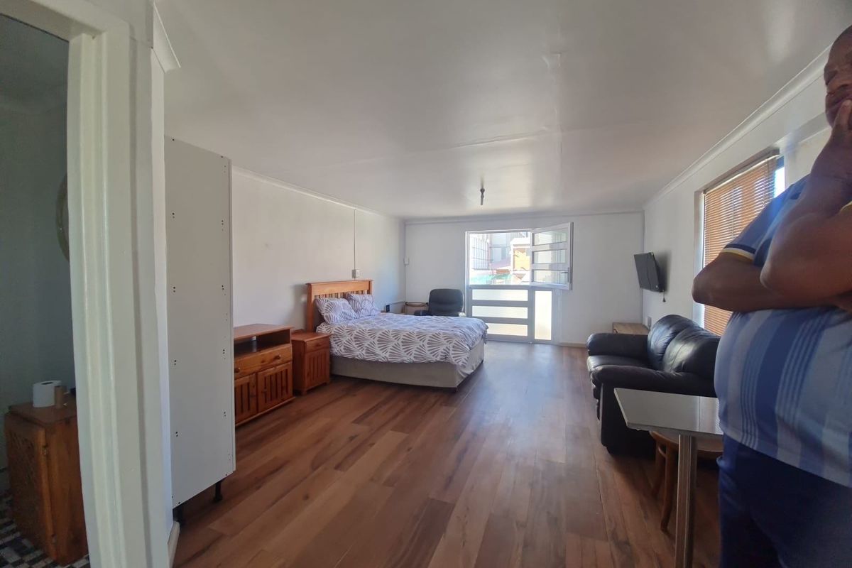 A spacious bedroom featuring wood-look flooring, neutral walls, and a large window providing natural light.