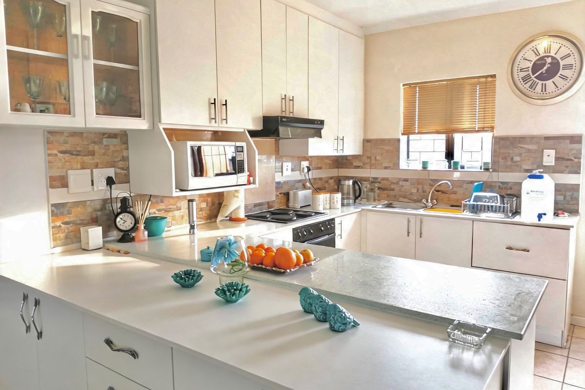 A functional kitchen featuring white cabinetry, stone-look tile backsplash, a breakfast bar, and integrated appliances including a hob and extractor fan.