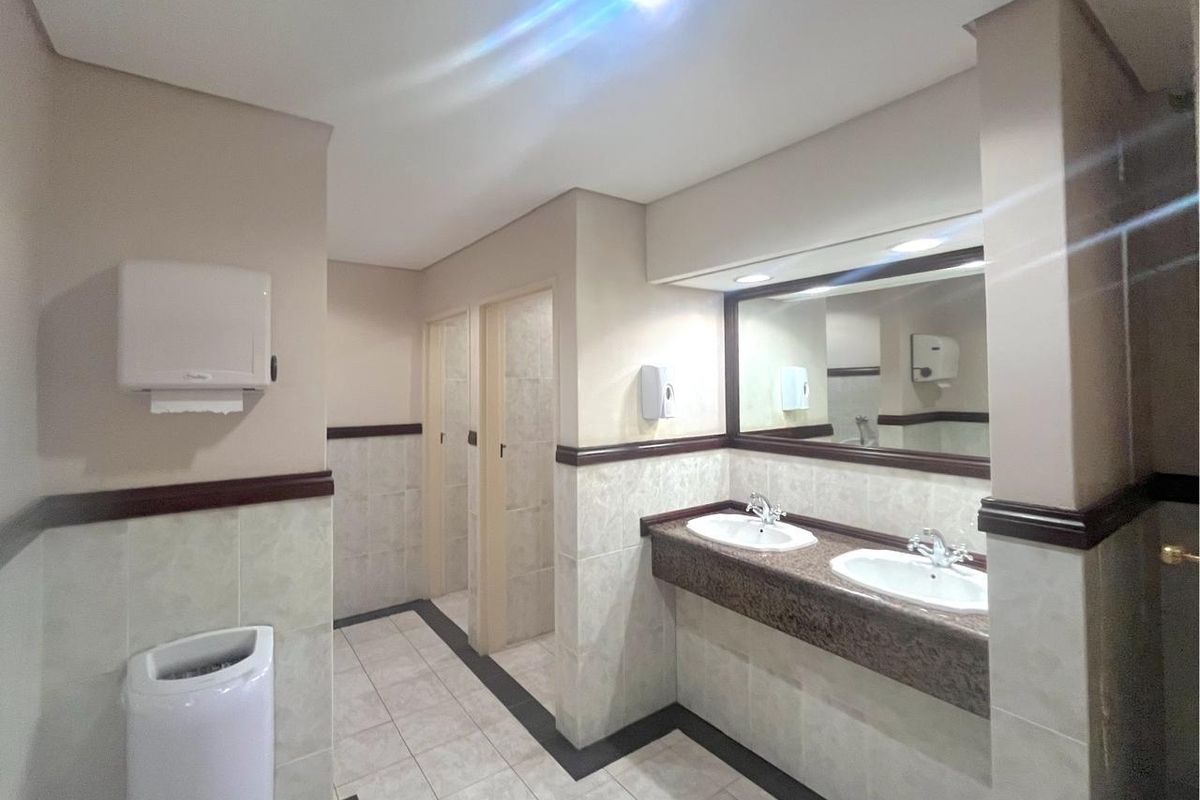 Commercial restroom facility featuring dual vanity sinks with granite countertops, tiled flooring, and separate partitioned cubicles.