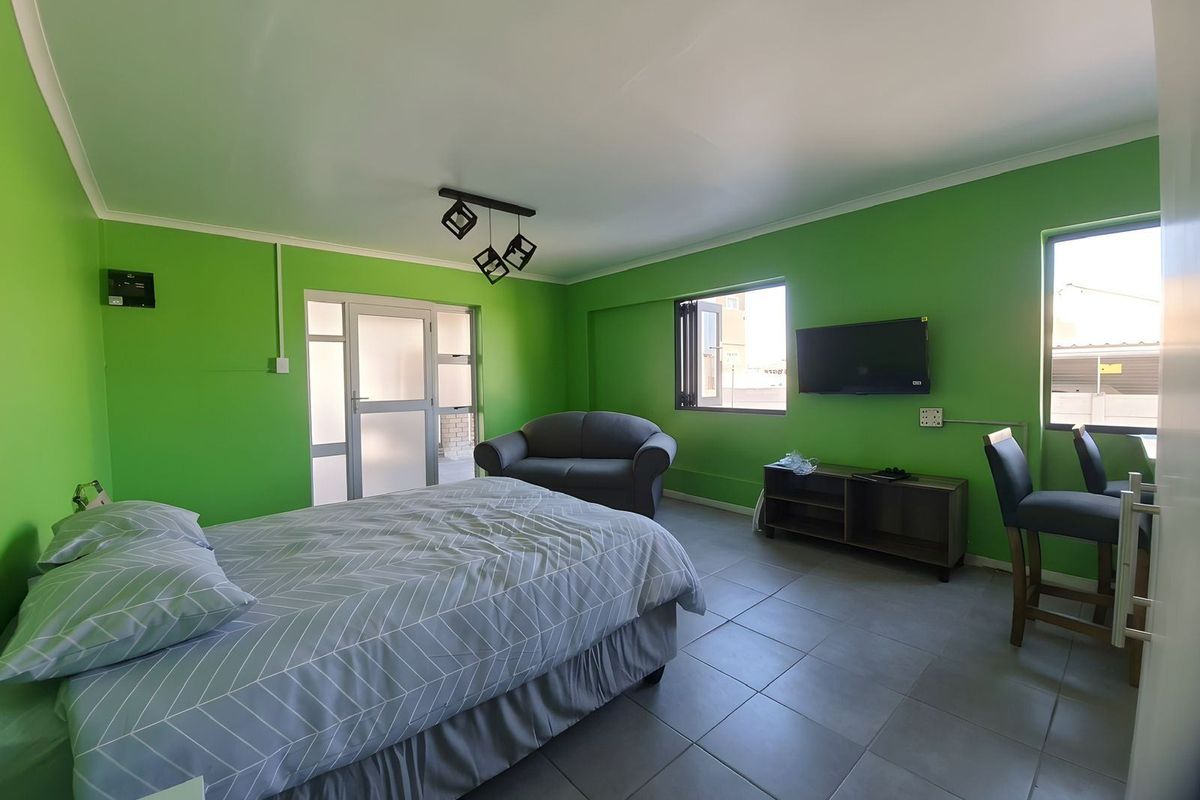 A bedroom featuring tiled flooring, large windows, and a glass-panelled door leading to an outdoor area, finished with bright green wall paint.