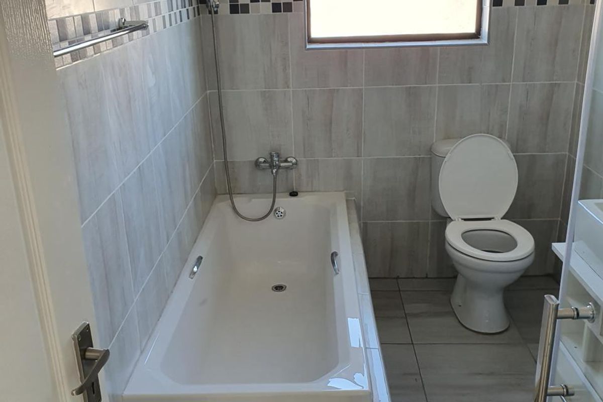 A functional bathroom featuring a built-in bathtub with shower attachment, a standard toilet, and neutral wall and floor tiling.