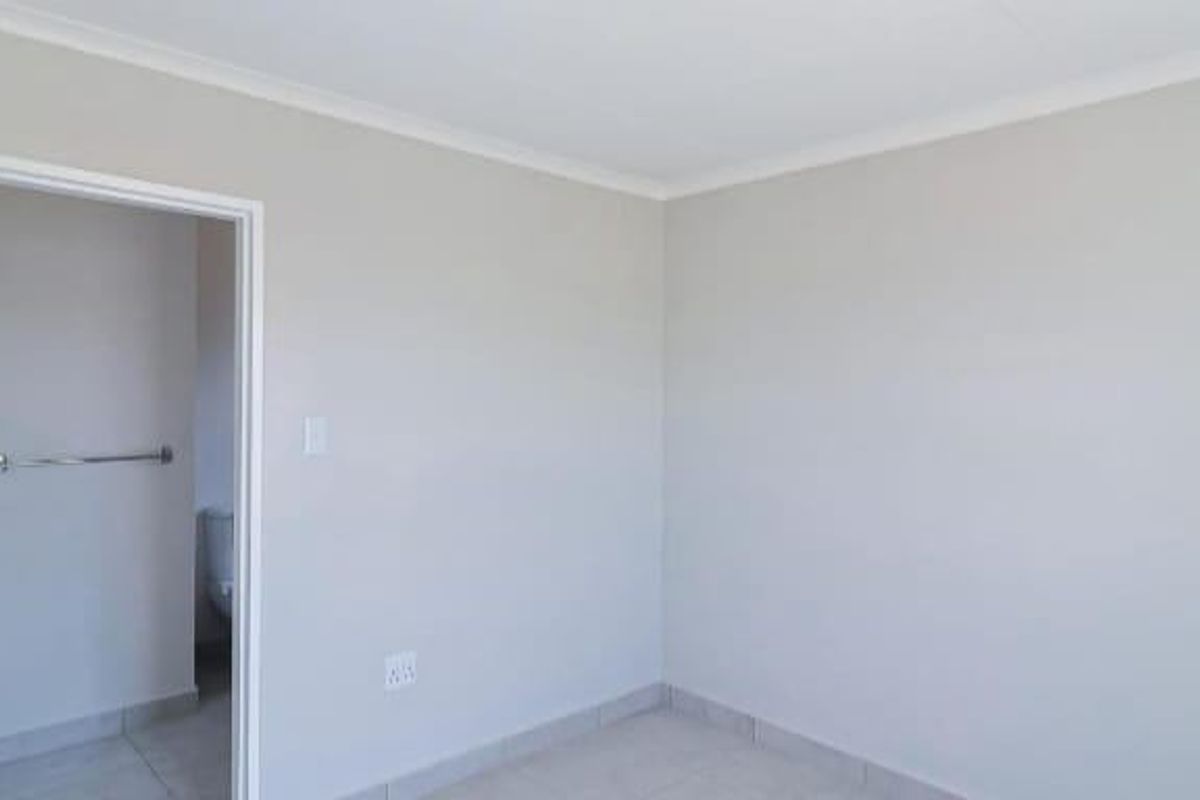 A clean, neutral-toned bedroom featuring tiled flooring and an adjoining en-suite bathroom with a towel rail.