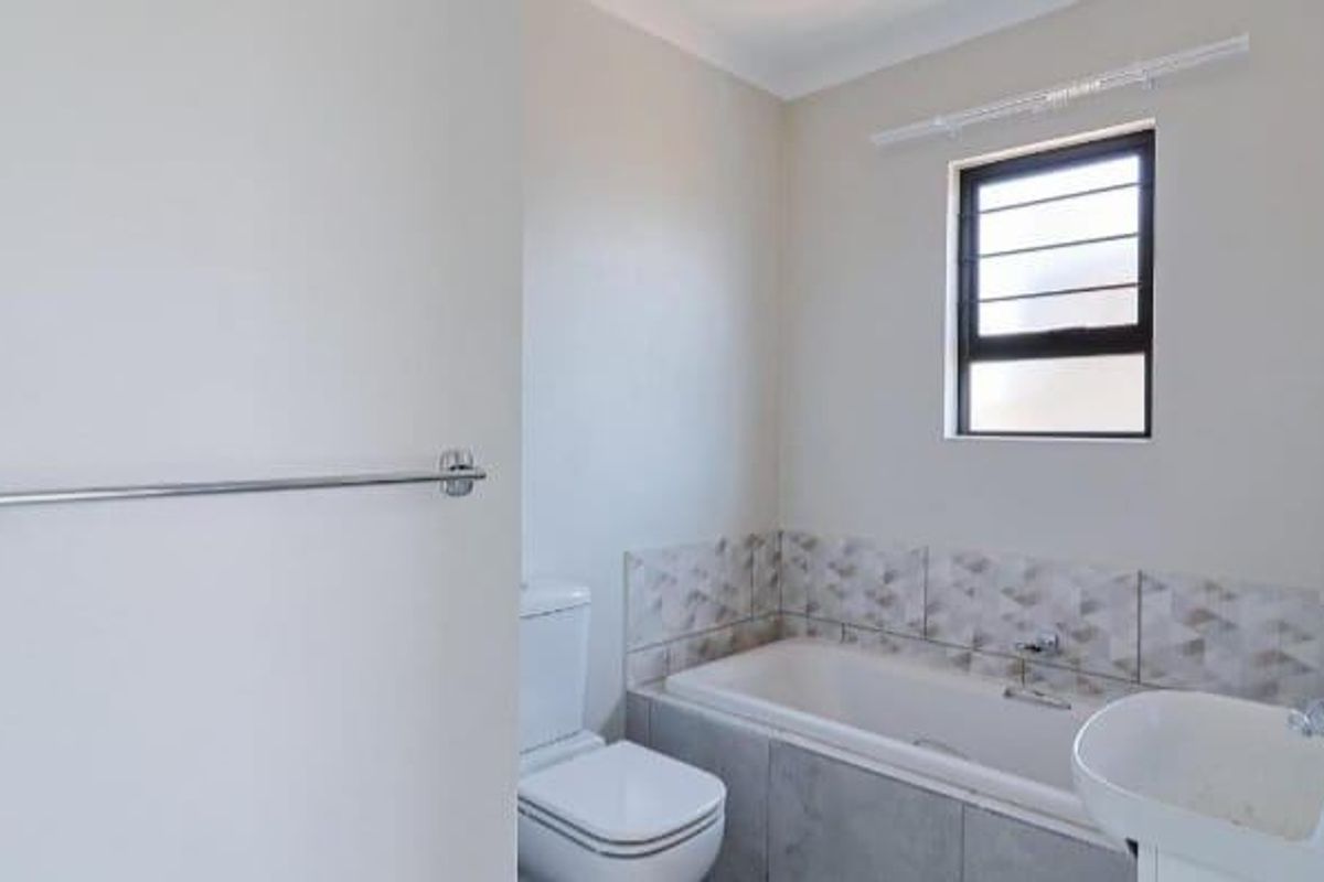 A clean, modern bathroom featuring a built-in bathtub, a wall-mounted toilet, a pedestal basin, and patterned wall tiling.