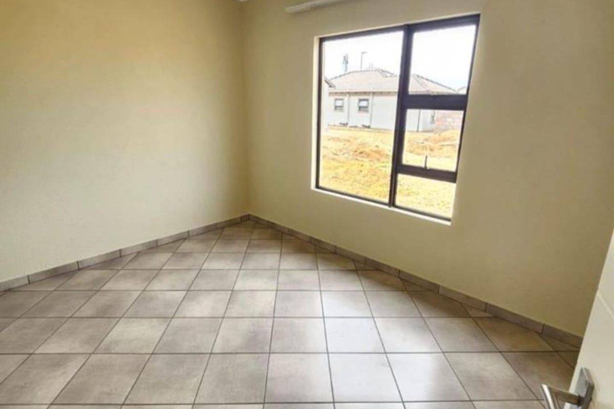 A clean, empty bedroom featuring neutral tiled flooring, painted walls, and a large window providing natural light.