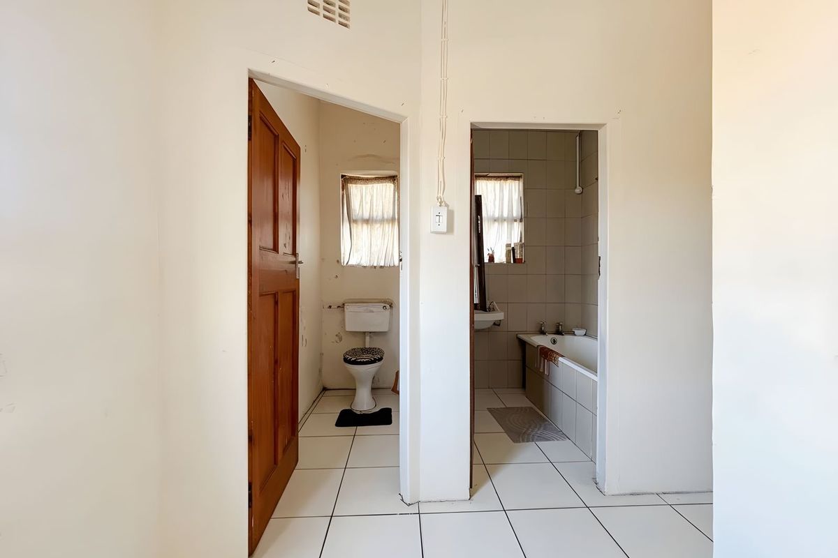 A view of a bathroom and separate toilet area featuring tiled flooring, a bathtub, and a wall-mounted toilet.
