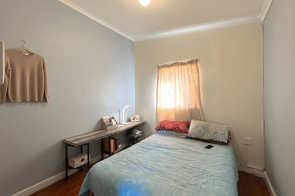 A compact bedroom featuring hardwood flooring, neutral wall tones, and a window with fitted curtaining.