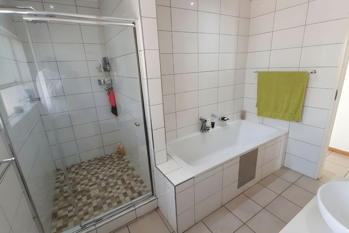 A functional bathroom featuring a glass-enclosed shower, a built-in bathtub with tiled surround, and a modern basin.