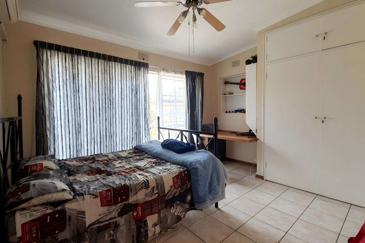 A functional bedroom featuring built-in cupboards, a recessed desk area, tiled flooring, and a ceiling fan.