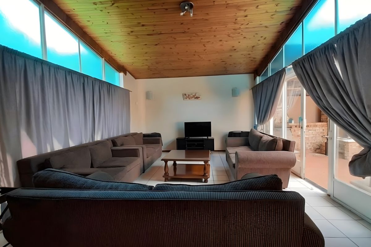 Spacious living room featuring a vaulted timber-clad ceiling, tiled flooring, and large windows with sliding door access to the outdoor patio area.