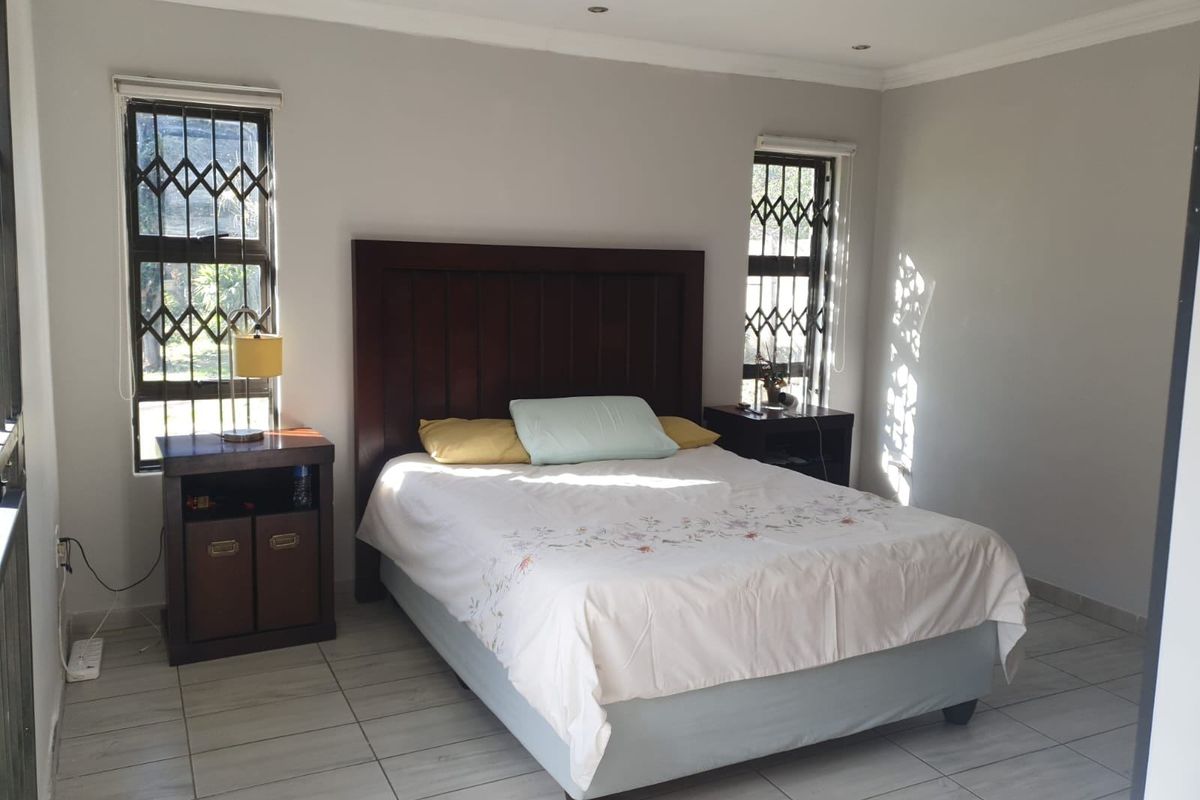 A bright bedroom featuring tiled flooring, recessed ceiling lighting, and security bars on the windows.