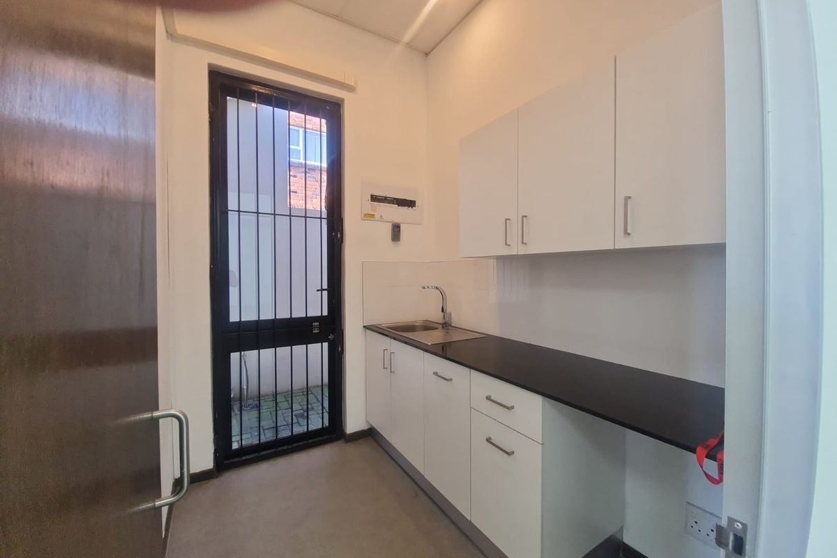 A functional kitchenette area featuring white cabinetry, a dark countertop, a stainless steel sink, and a security door leading to an outdoor space.