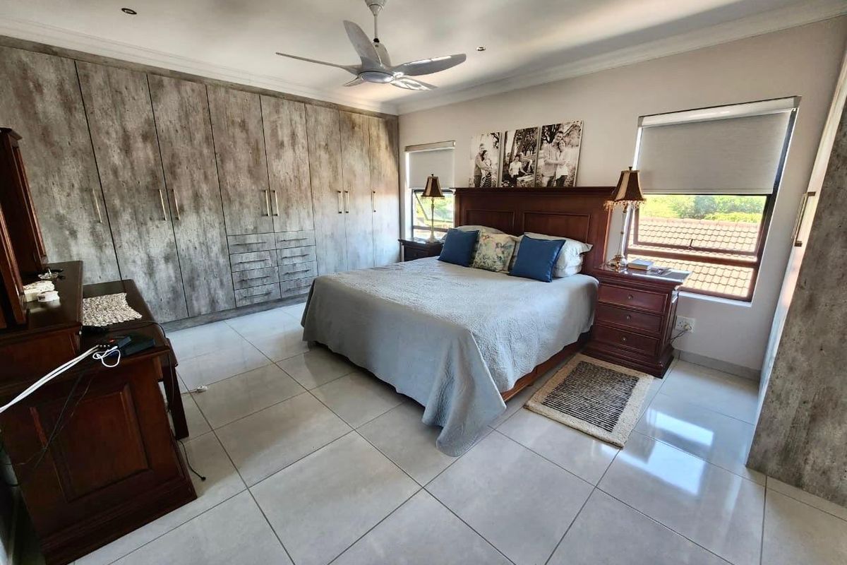 Spacious bedroom featuring large built-in cupboards with a textured finish, tiled flooring, ceiling fan, and roller blinds.