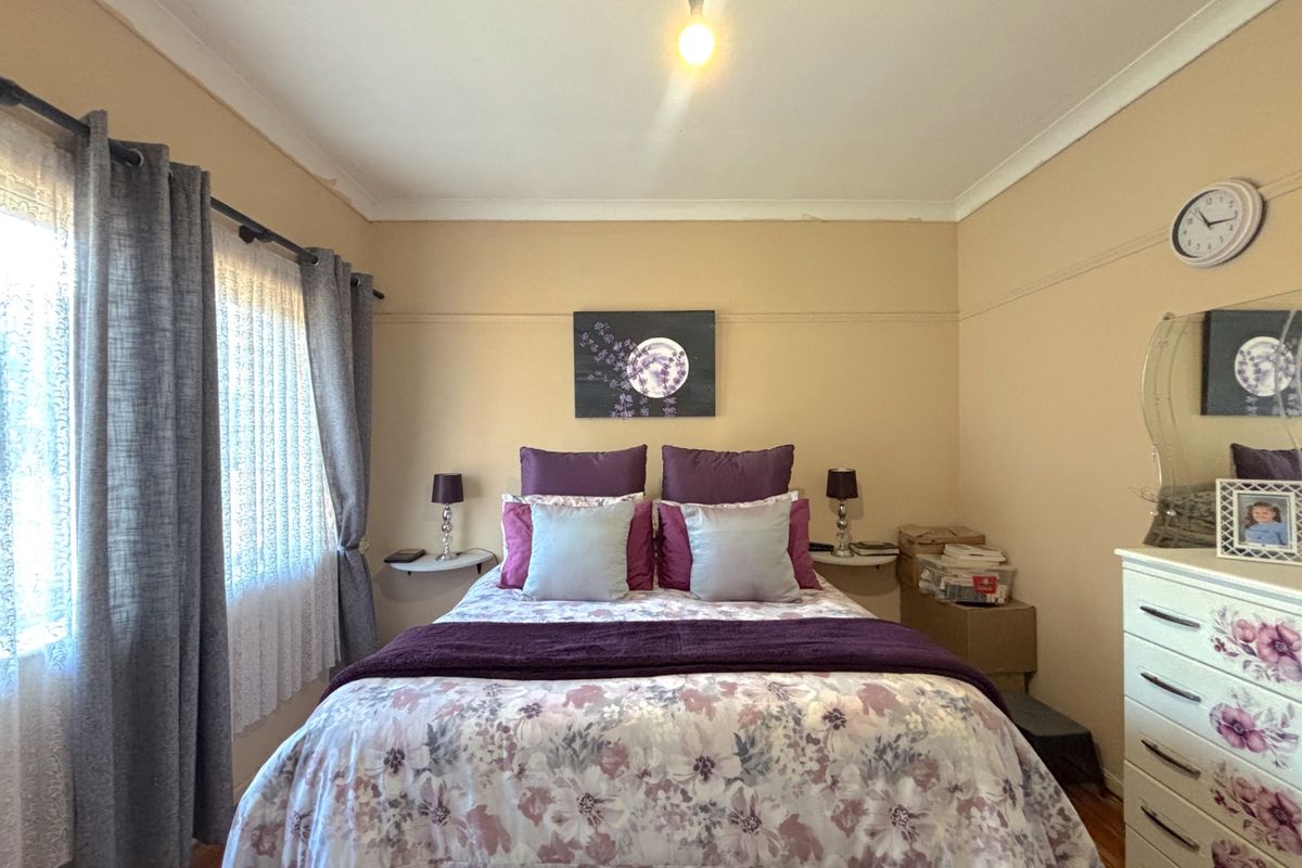 A cozy bedroom featuring timber flooring, neutral wall tones, and a window with curtain treatments, providing a comfortable and functional sleeping space.