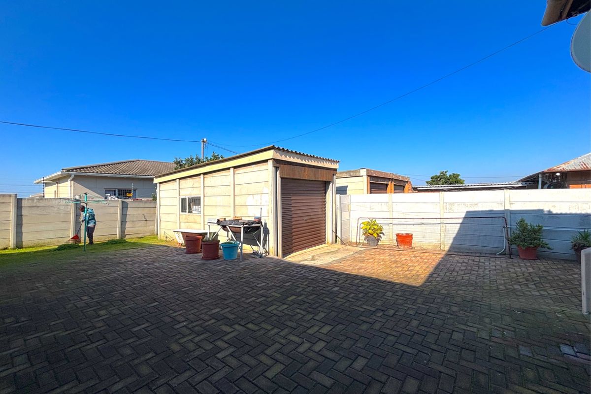 A paved rear yard featuring a detached garage structure with a roller door and perimeter precast concrete walling.