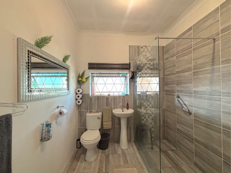 Modern bathroom featuring a glass-enclosed walk-in shower, pedestal sink, and tiled flooring with neutral wall finishes.