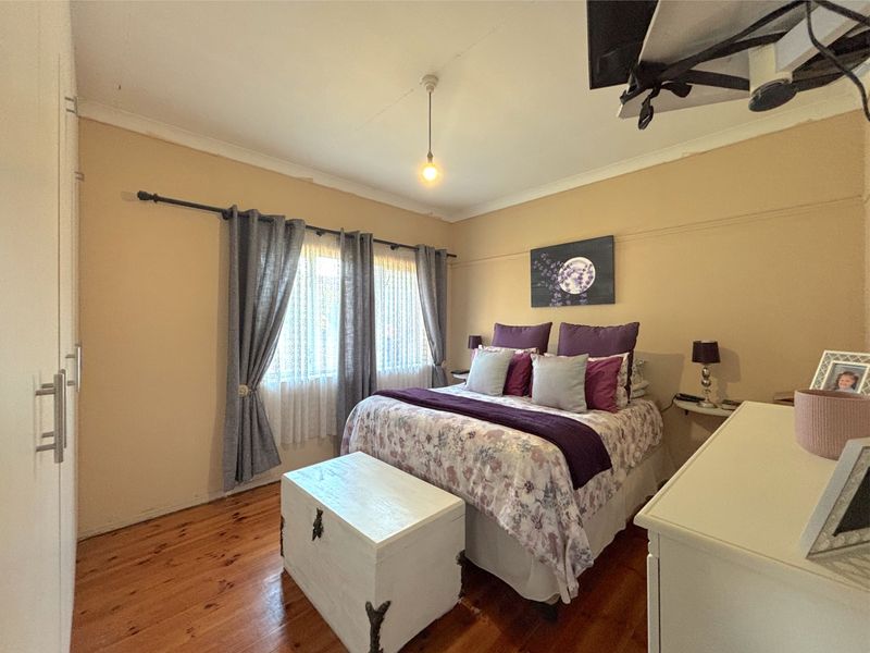 A cozy bedroom featuring polished timber flooring, built-in wardrobe storage, and a classic picture rail detail.