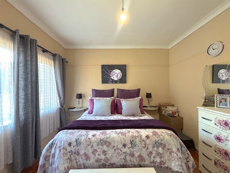 A cozy bedroom featuring timber flooring, neutral wall tones, and a window with curtain treatments, providing a comfortable and functional sleeping space.