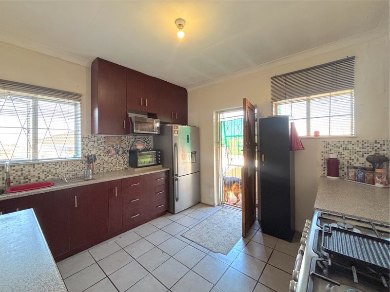Functional kitchen featuring dark wood cabinetry, tiled countertops, mosaic backsplash, and direct access to the exterior.