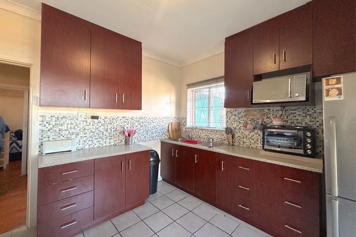 A functional kitchen featuring dark wood cabinetry, a mosaic tile backsplash, laminate countertops, and tiled flooring.