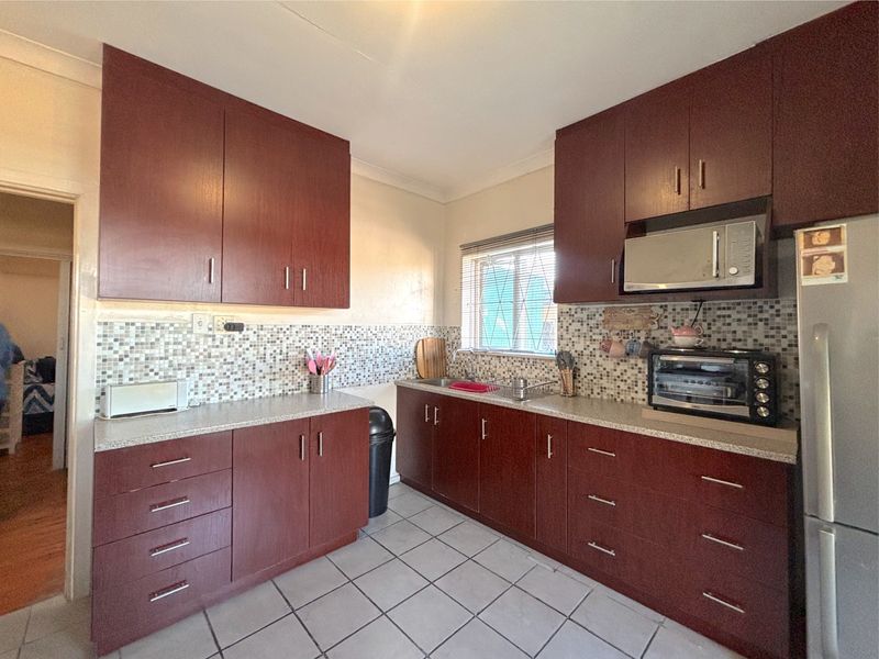 A functional kitchen featuring dark wood cabinetry, a mosaic tile backsplash, laminate countertops, and tiled flooring.