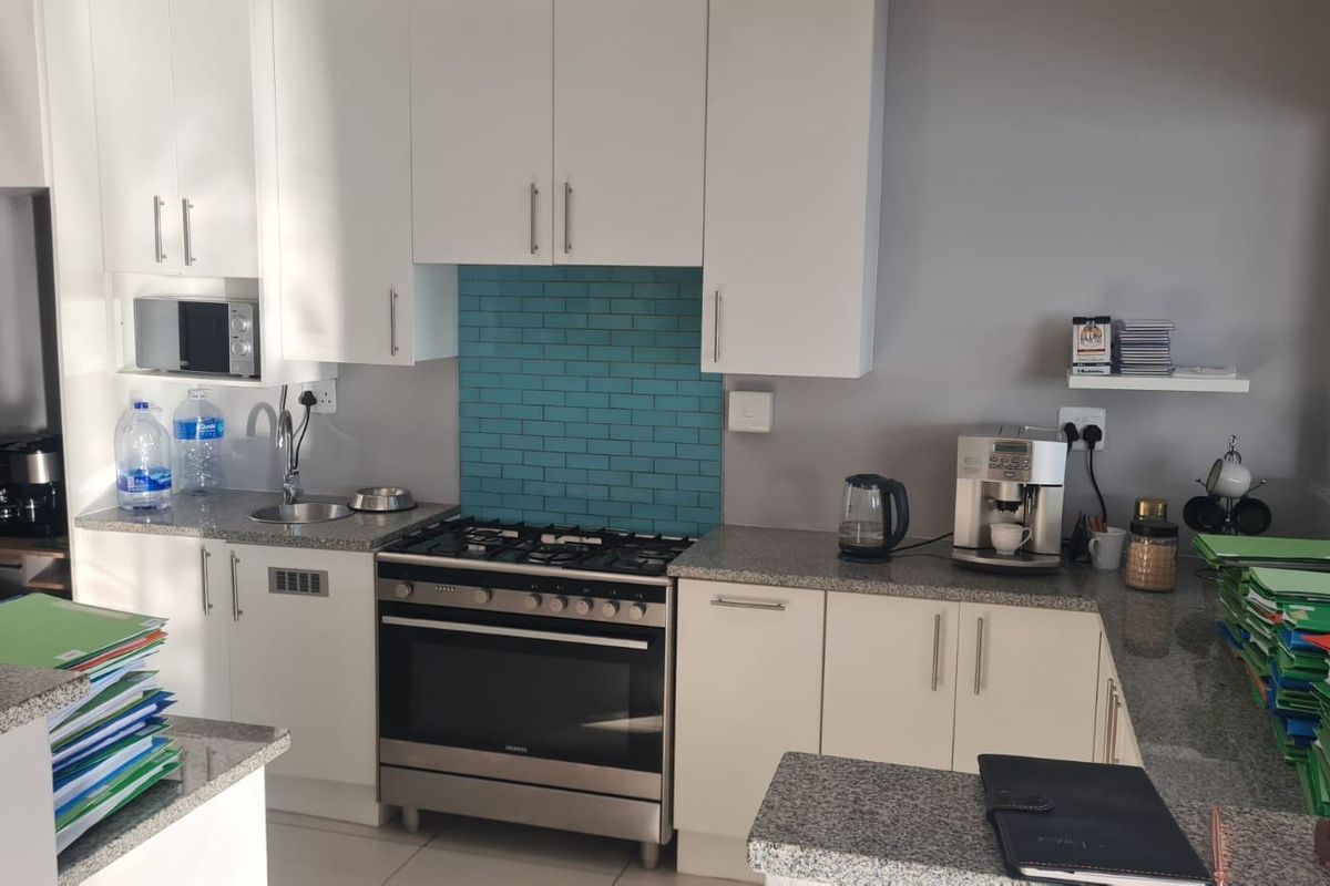A functional kitchen featuring white cabinetry, granite countertops, a stainless steel gas stove with oven, and a vibrant blue subway tile backsplash.