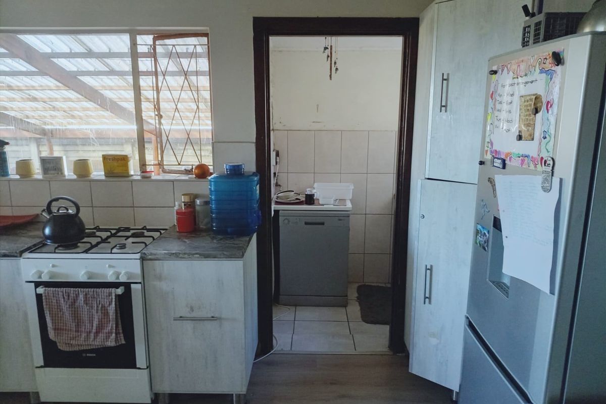A functional kitchen featuring built-in cabinetry, a gas stove, and an adjacent scullery area with tiled flooring and splashbacks.