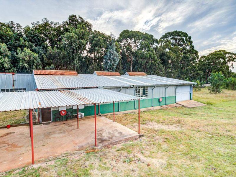 Exterior view of a large farm outbuilding featuring a corrugated metal roof, attached covered patio area, and expansive surrounding grounds.