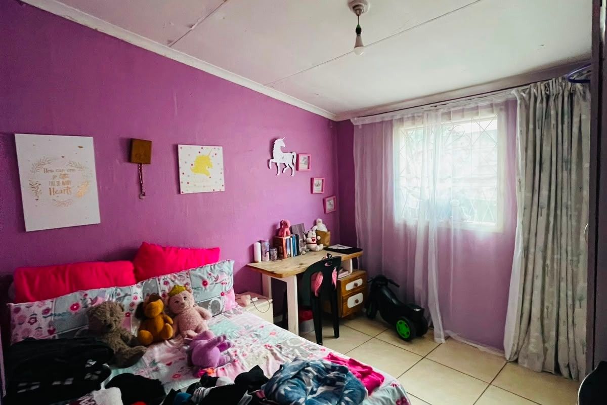 A bedroom featuring tiled flooring and a window with curtain treatments, currently utilized as a child's room.
