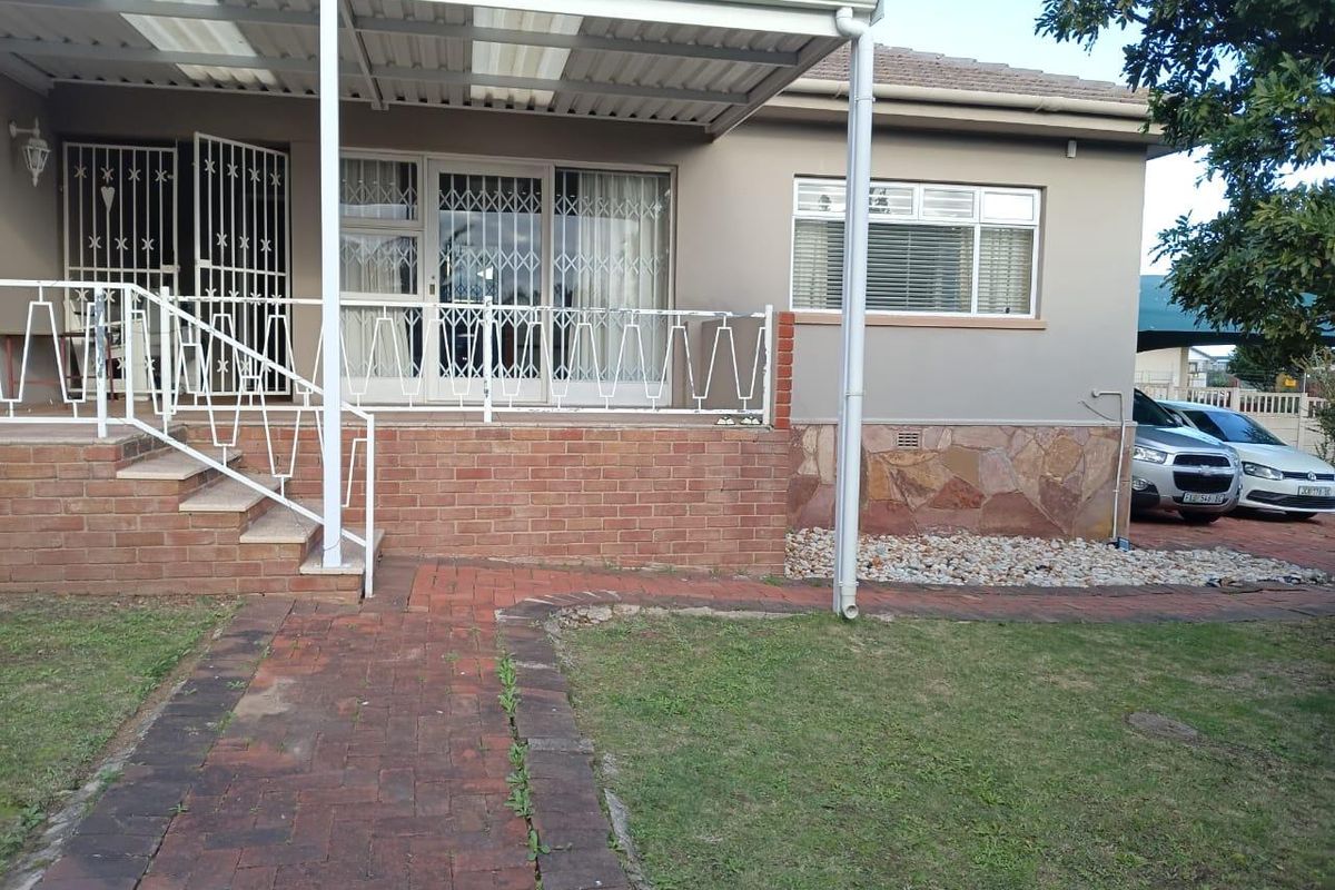 Rear exterior view featuring a covered patio with brick stairs, stone cladding accents, and a paved walkway leading to the garden area.