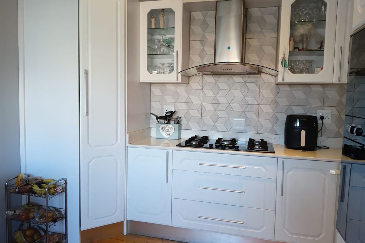 A well-maintained kitchen featuring white cabinetry, a modern gas hob with extractor fan, and a stylish geometric tiled backsplash.