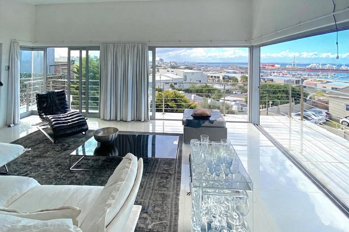 Spacious living area featuring floor-to-ceiling glass sliding doors that open onto a balcony with expansive harbour and city views.