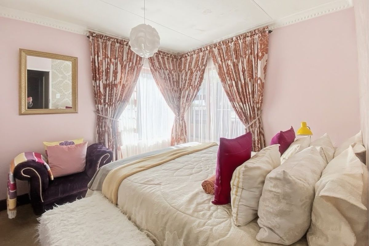 A cozy bedroom featuring decorative crown molding, large windows with curtains, and neutral carpeting.