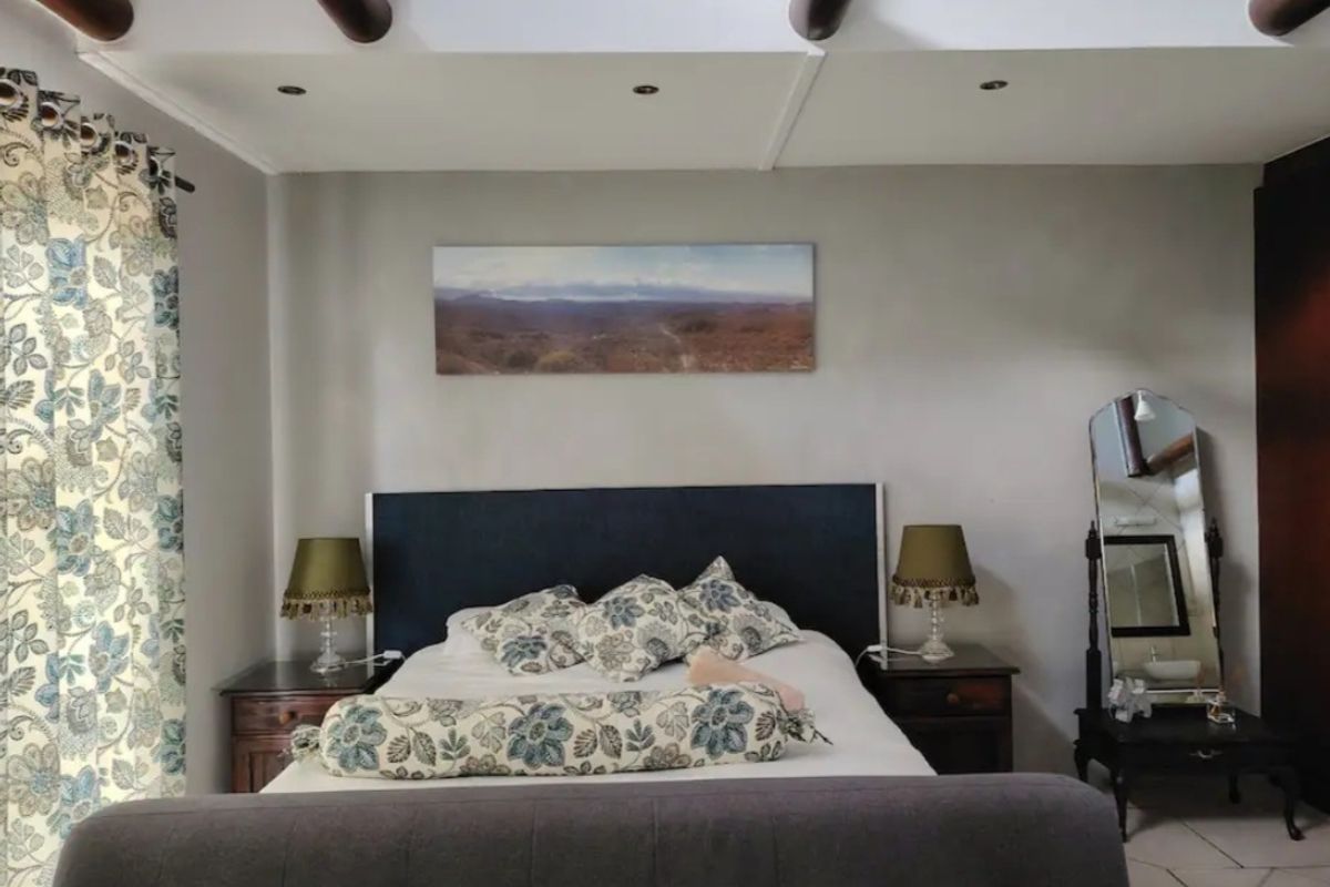 A well-maintained bedroom featuring exposed timber ceiling beams, recessed downlighting, and neutral wall finishes with tiled flooring.