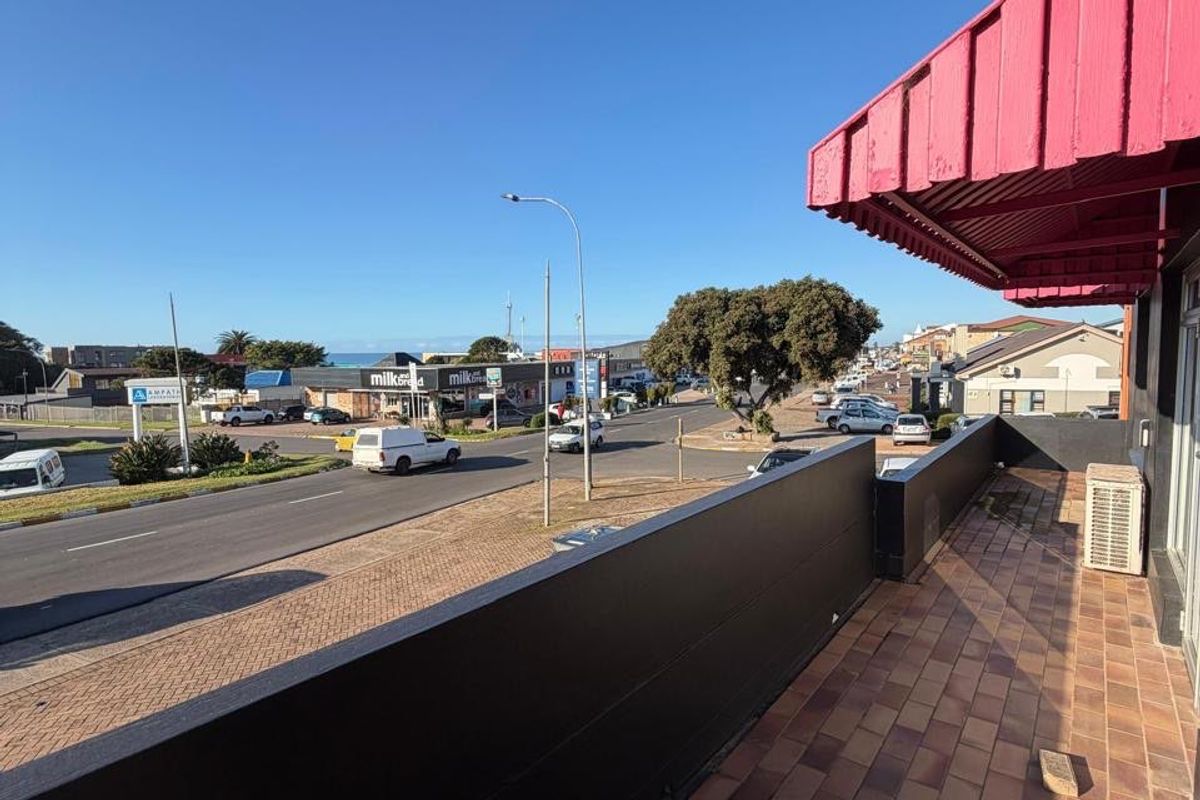 A commercial balcony area featuring tiled flooring, a protective metal awning, and an exterior air conditioning unit, overlooking a busy street.