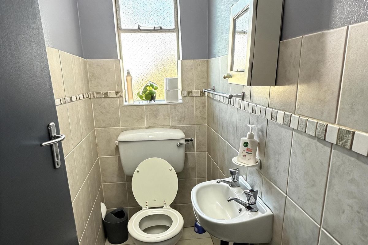 A compact guest bathroom featuring a wall-mounted basin, toilet, tiled walls, and a small window providing natural light.