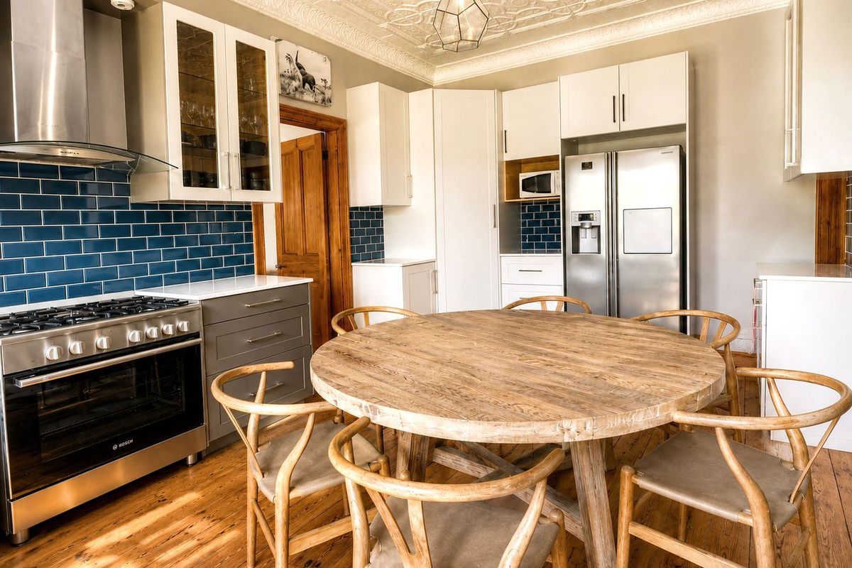 A well-appointed kitchen featuring a gas range, stainless steel extractor fan, blue subway tile backsplash, and decorative pressed metal ceiling.