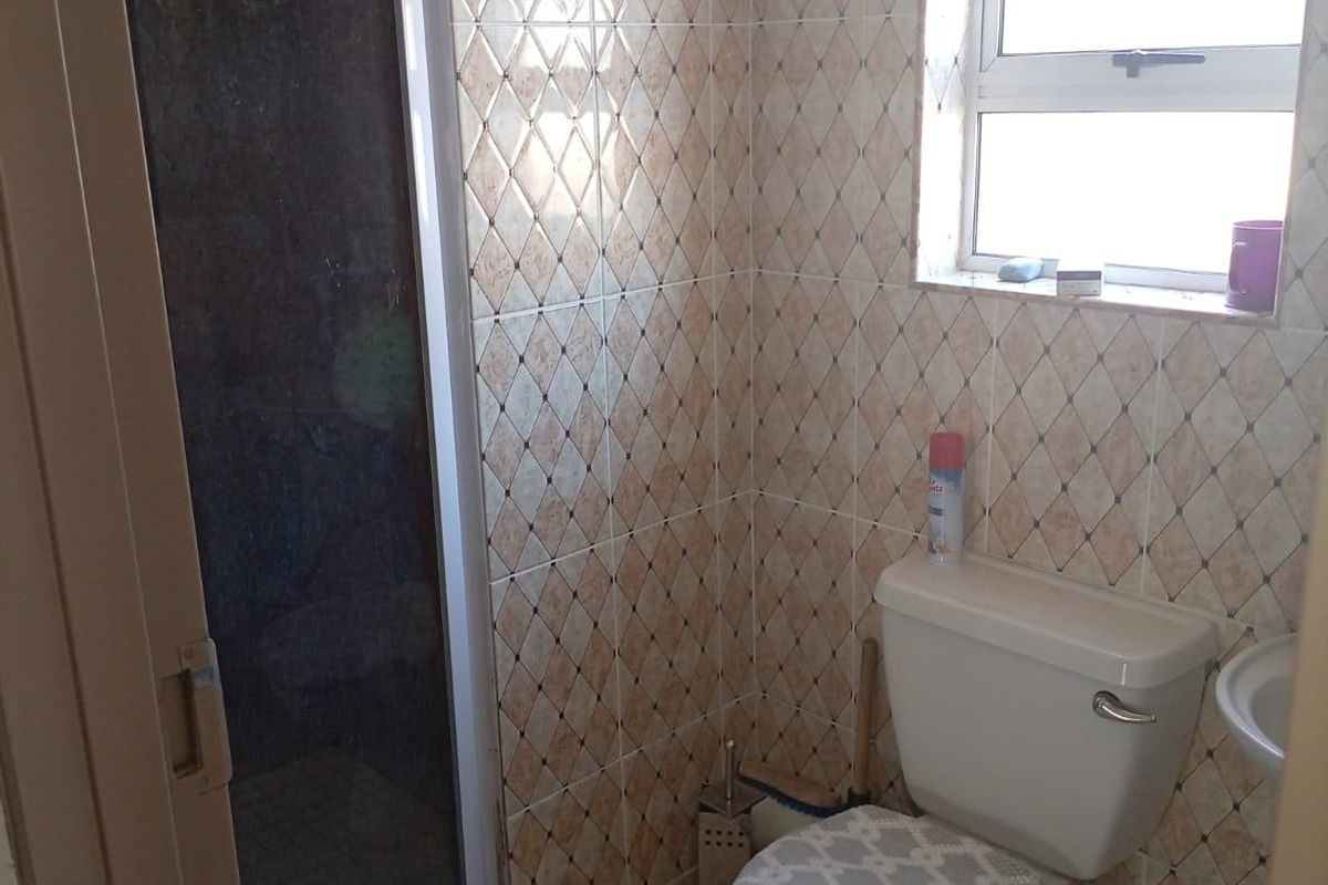A compact bathroom featuring a shower enclosure, toilet, and window, finished with dated wall tiles and neutral floor tiling.