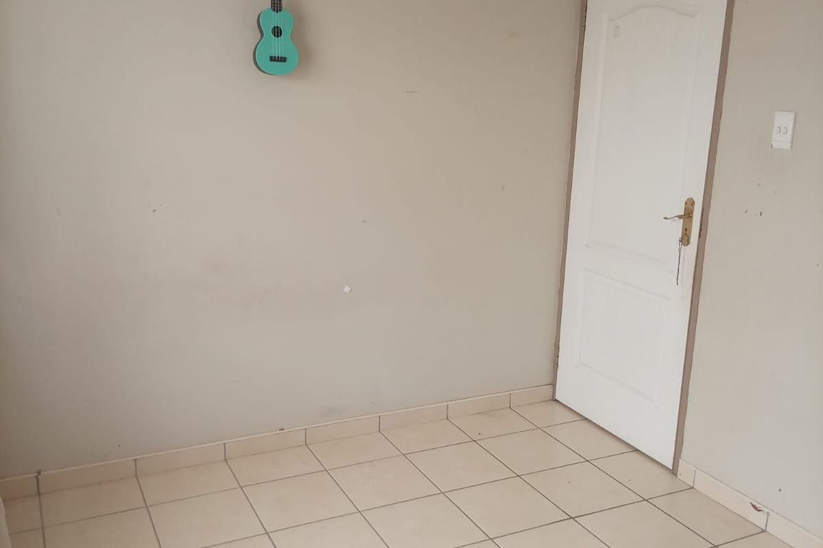 A simple, tiled interior room featuring neutral wall tones and a single access door, suitable for use as a bedroom or study.