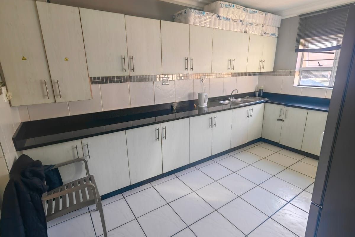 A functional kitchen featuring white laminate cabinetry, dark granite countertops, a stainless steel sink, and tiled flooring with a neutral backsplash.