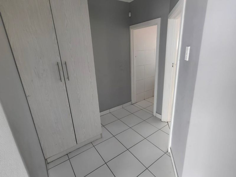 A clean, neutral hallway featuring light-toned built-in cupboards, white tiled flooring, and classic ceiling cornicing.