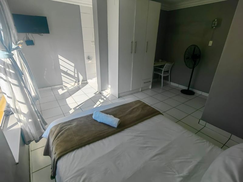 A bedroom featuring tiled flooring, a ceiling fan, and a built-in wardrobe, with visible signs of wear on the ceiling and floor.