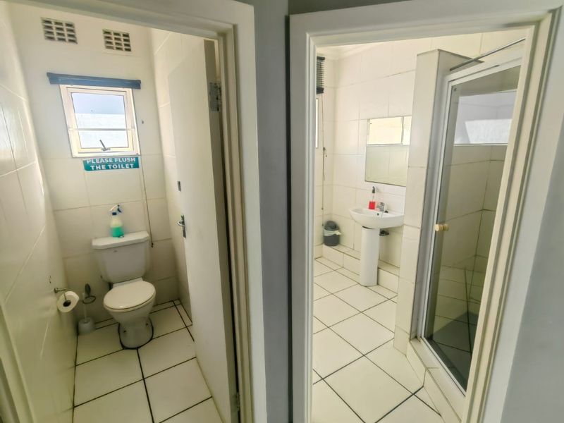 A functional commercial bathroom suite featuring a separate toilet cubicle and a shower area with a pedestal basin.